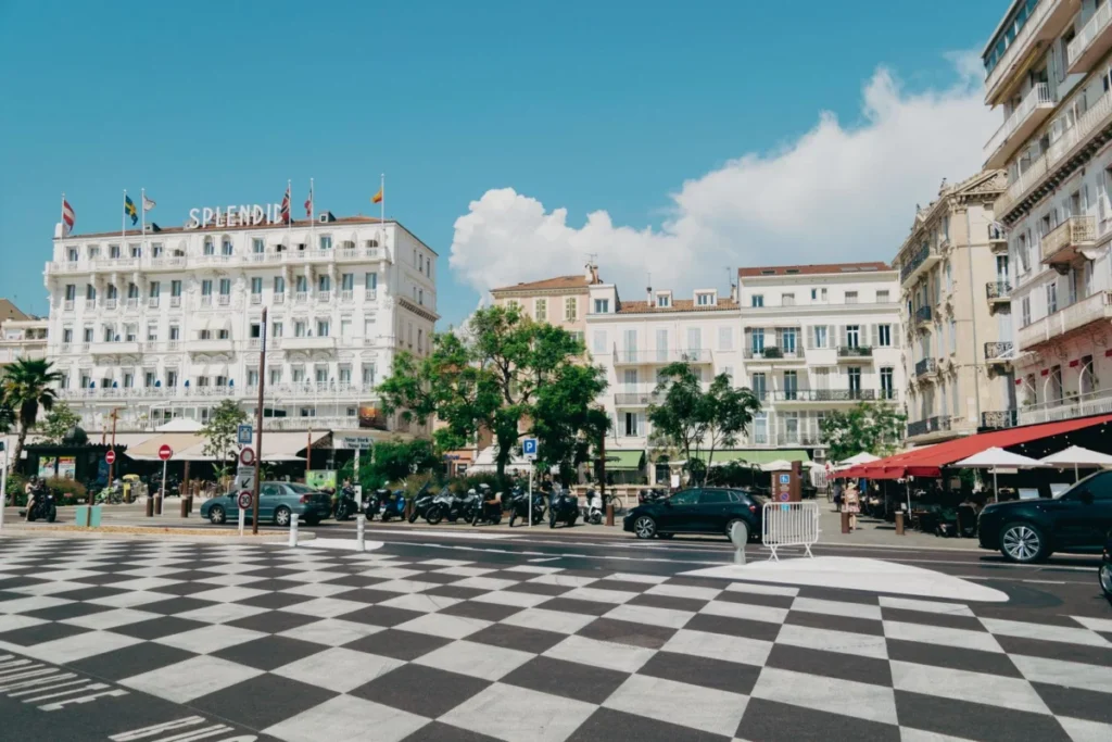 Busy central square in Cannes with hotels, café terraces and parked cars on a summer day