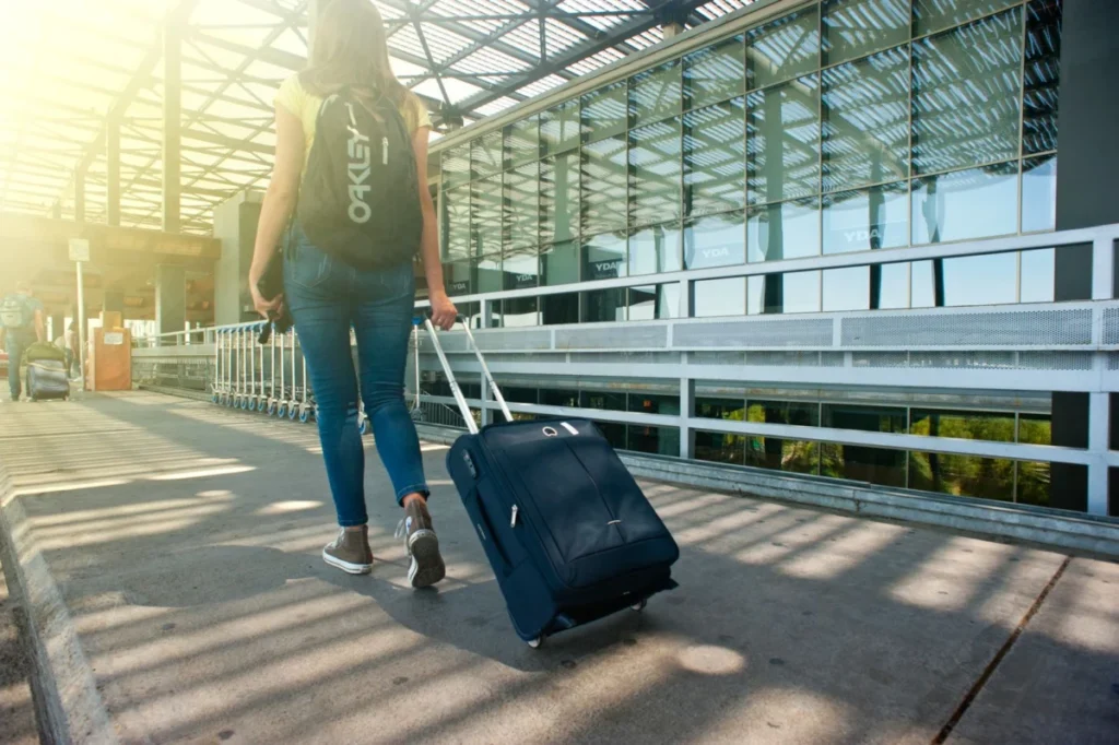 Traveller pulling a suitcase outside an airport terminal, heading to the ride app pickup area
