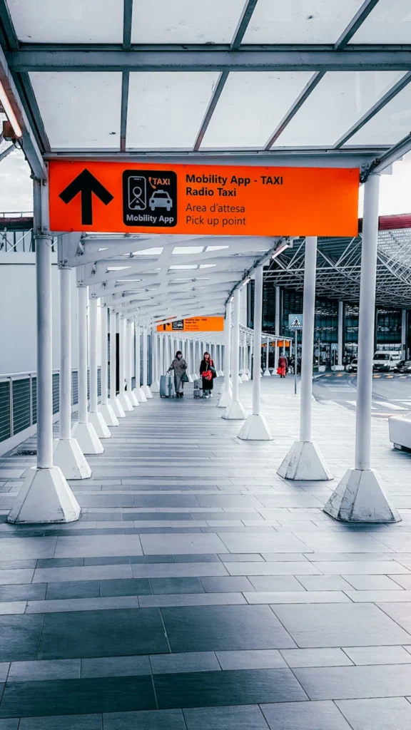 Covered airport walkway with an orange sign pointing travellers to the ride app pick-up point