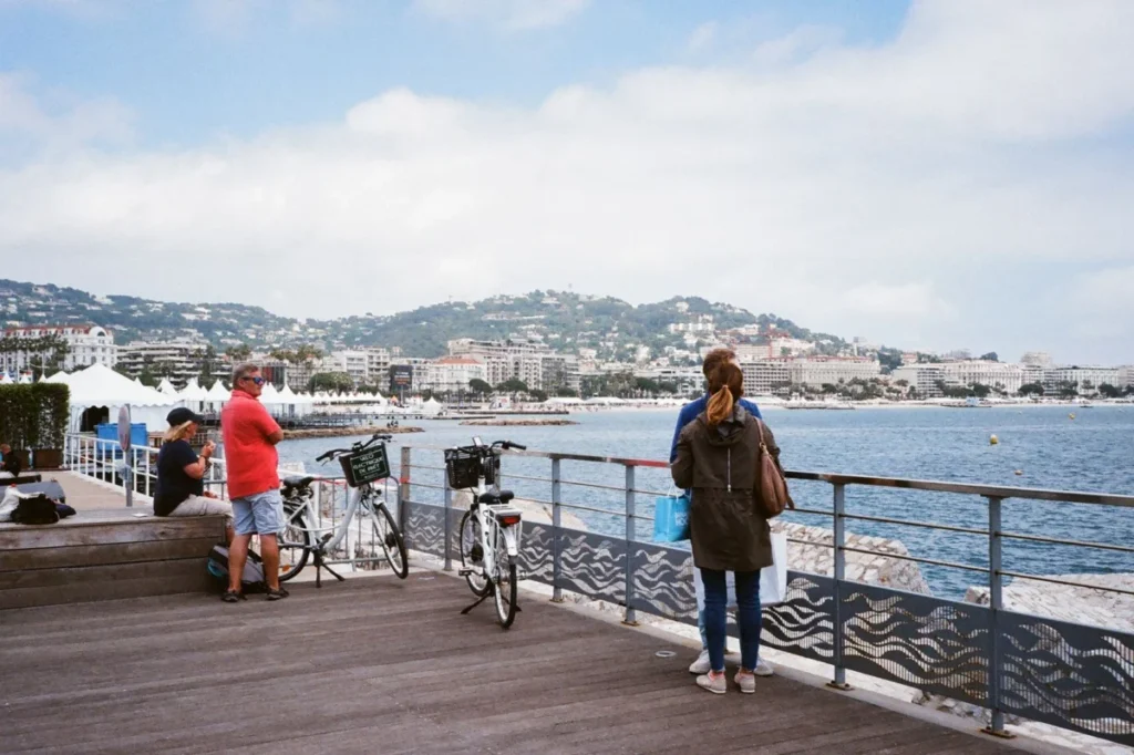 Visitors with bikes and bags on a seafront jetty in Cannes, overlooking the bay